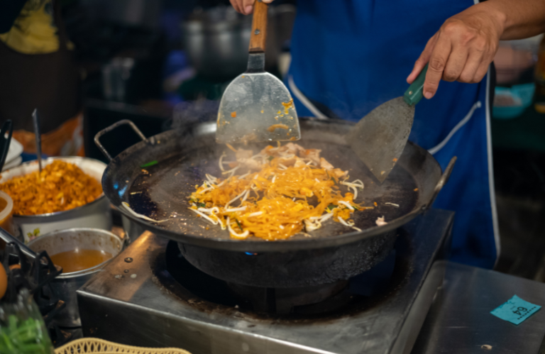 person frying noodles in a pan thai street food